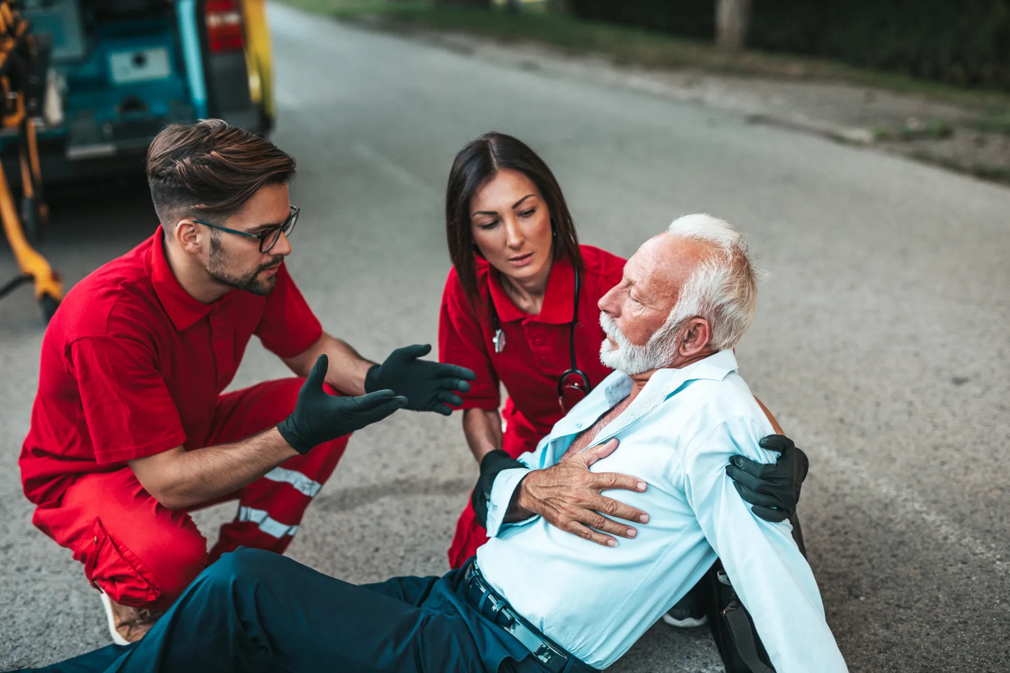 Two paramedics kneeling down to treat a man who is grasping his chest