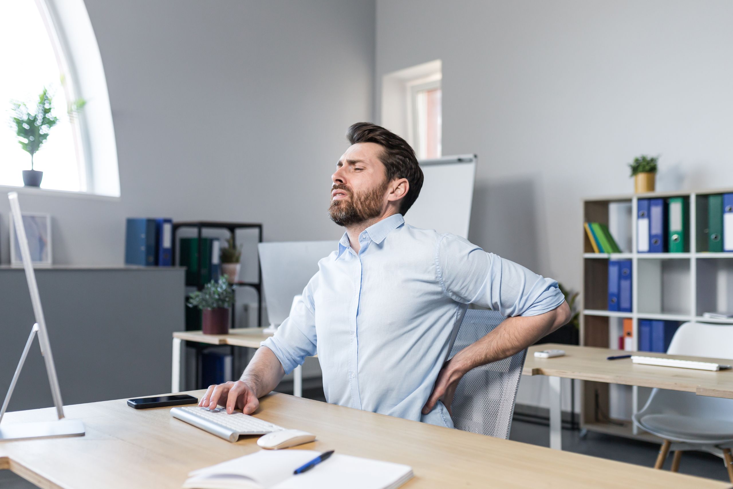 A man sitting at his desk, clenching his lower back in pain